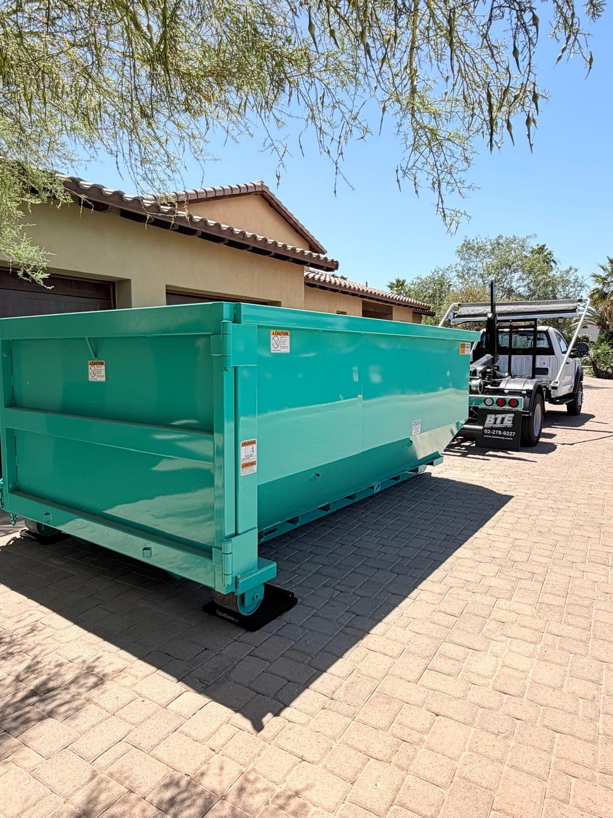 East Valley Bin Co. roll-off truck placing a teal 15-yard dumpster for a garage cleanout job in the East Valley, Arizona