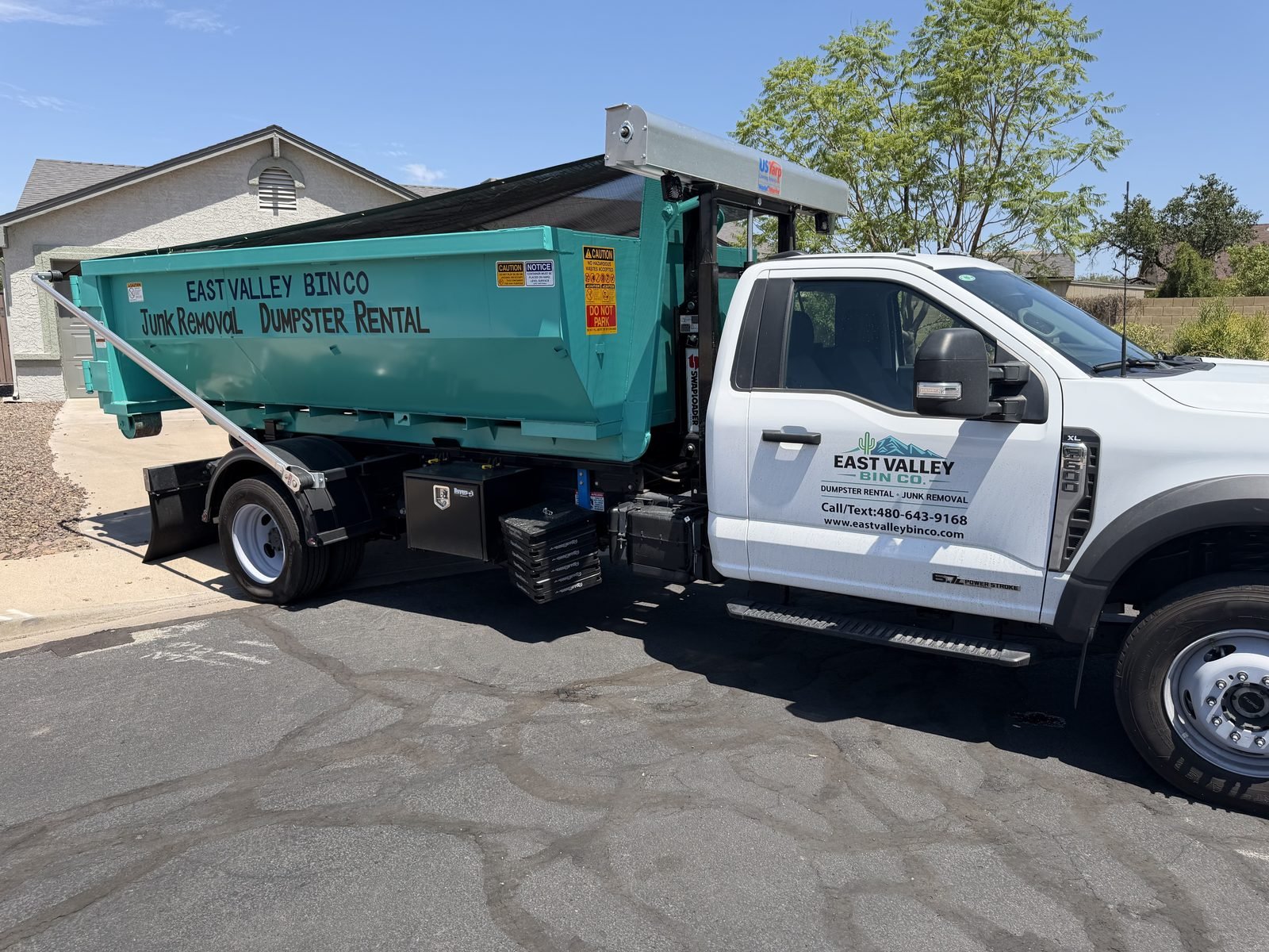 East Valley Bin Co. branded roll-off truck delivering a teal dumpster at a home in the East Valley, Arizona